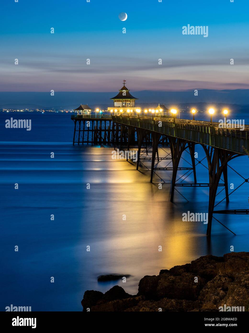 Una luna a mezzaluna si tramonta sul canale di Bristol e sul molo di Clevedon al tramonto a Somerset, Inghilterra. Foto Stock