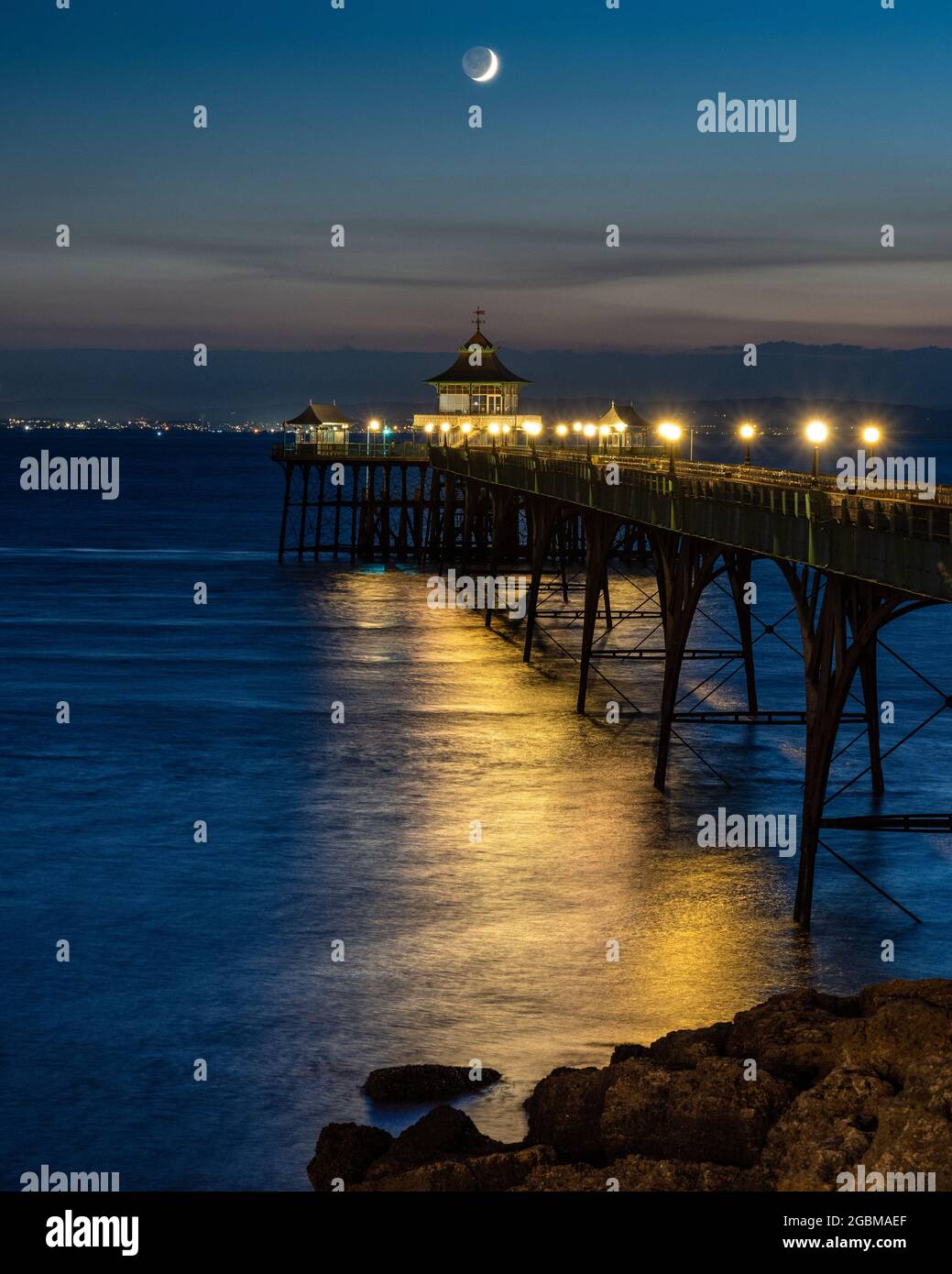 Una luna a mezzaluna si tramonta sul canale di Bristol e sul molo di Clevedon al tramonto a Somerset, Inghilterra. Foto Stock