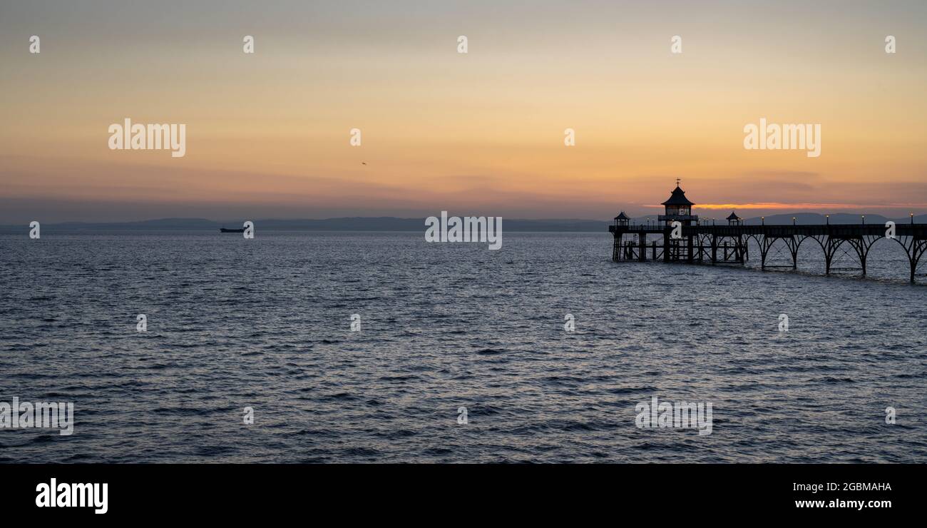 Una nave da carico viaggia oltre il molo di Clevedon nel canale di Bristol al tramonto. Foto Stock