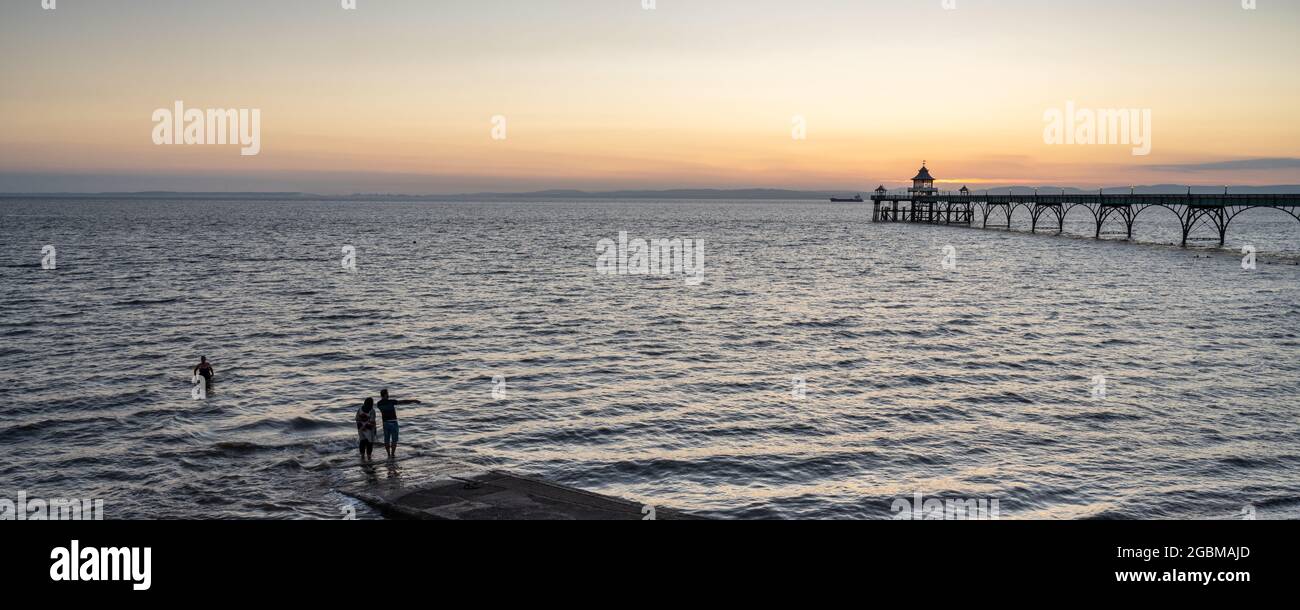 Le persone si bagnano e pagaiano nel canale di Bristol accanto al molo di Clevedon al tramonto a Somerset, Inghilterra. Foto Stock