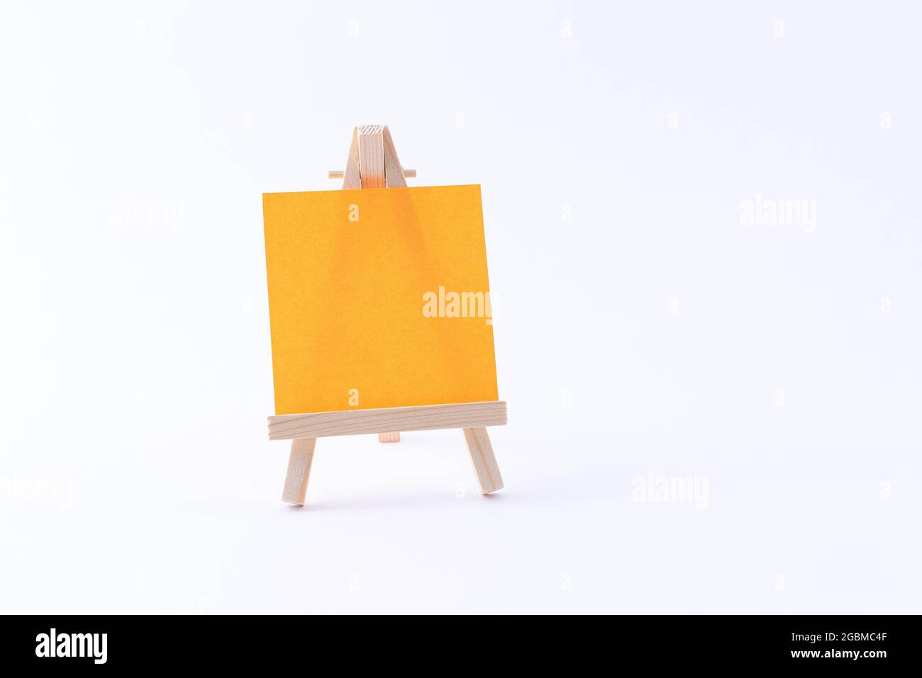 Easel in legno in miniatura con tela quadrata colorata vuota o carta Memo - Mockup. Mini supporto in legno con tavola da disegno pulita su sfondo bianco, spazio per la copia Foto Stock