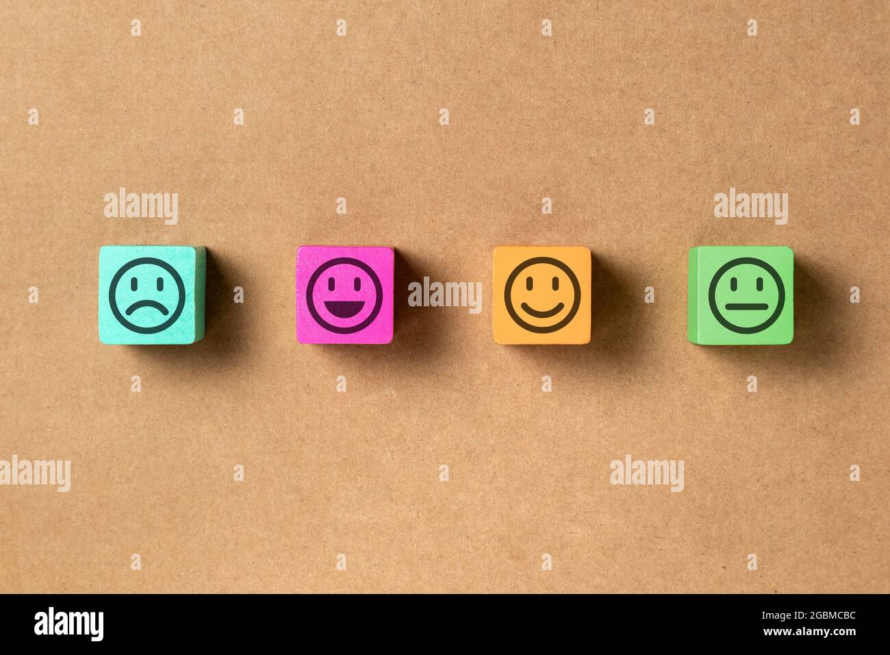 Emoticon facce in colori blocchi di legno su carta marrone. Valutazione del servizio e analisi della soddisfazione. Arrabbiato, neutro, buon umore e felice. COP Foto Stock