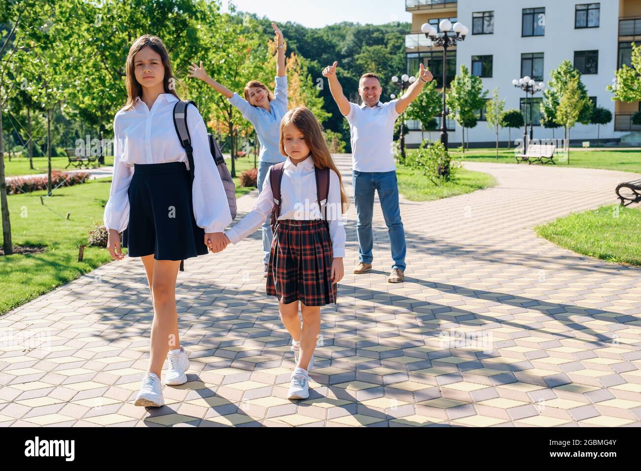 Due sorelle ragazze tengono le mani e vanno a scuola mentre i loro genitori gioiscono Foto Stock