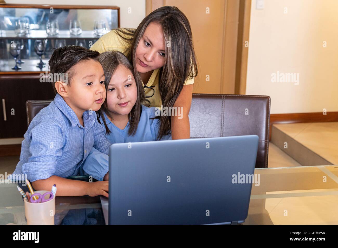 Una madre con il suo bambino maschio e la figlia femmina guarda il computer nella sala da pranzo facendo i compiti online Foto Stock