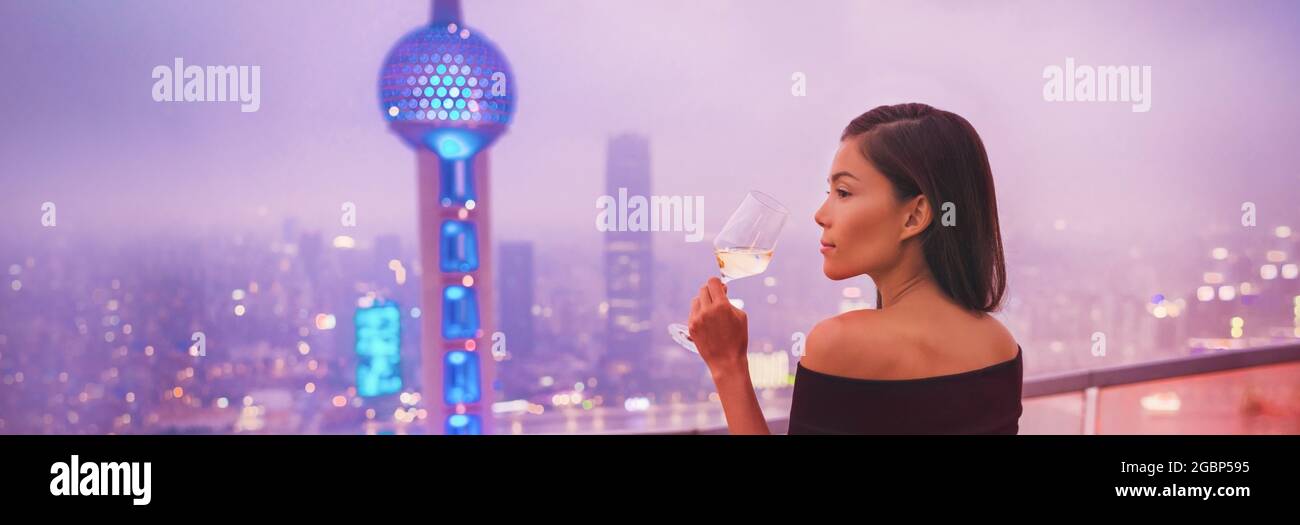 Lusso Shanghai stile di vita asiatica donna bere vino bianco in su China Travel. Modello elegante in abito nero su terrazza vista della città, di alta classe Foto Stock