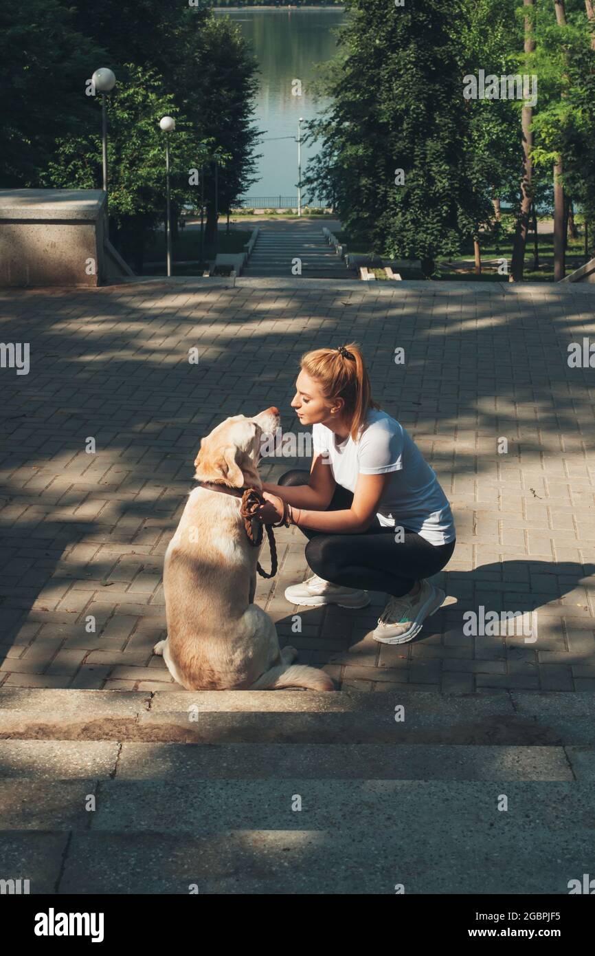 Indietro guarda la foto di una bionda caucasica che bacia il suo retriever d'oro durante una passeggiata nel parco Foto Stock