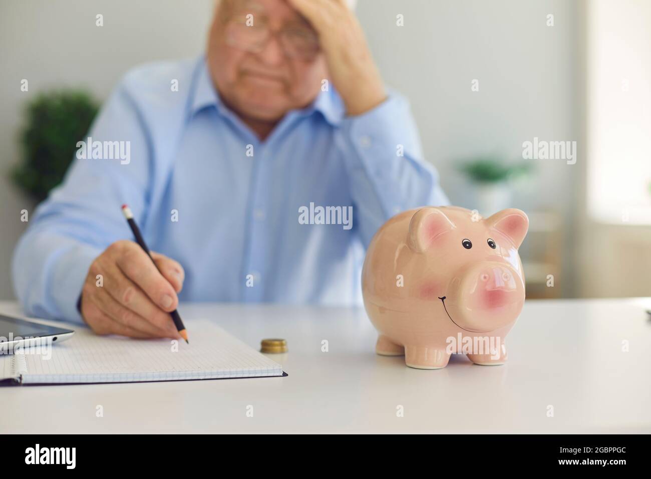 La banca del piggy si trova nel mezzo di un tavolo vicino ad un uomo anziano che sta prendendo le note in un taccuino. Foto Stock