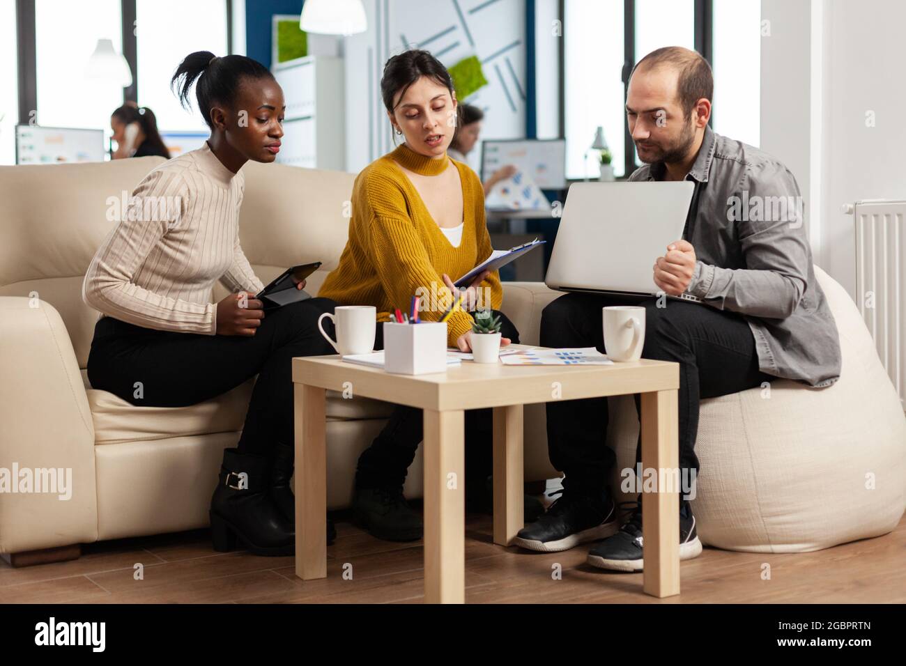 Team di colleghi creativi e amichevoli che discutono del progetto aziendale utilizzando notebook e tablet sul posto di lavoro. Gruppo di collaboratori multirazziali che lavorano insieme condividendo idee di marketing durante la riunione d'ufficio Foto Stock