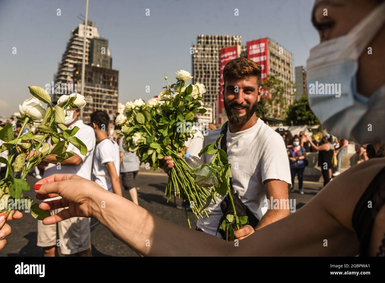 Beirut, Libano, 4 agosto 2021. Un uomo consegna fiori a persone che protestano per non aver trovato i responsabili del Beirut Blast e li rende responsabili di fronte a edifici danneggiati durante l'esplosione, ancora non riparati un anno dopo. Foto Stock