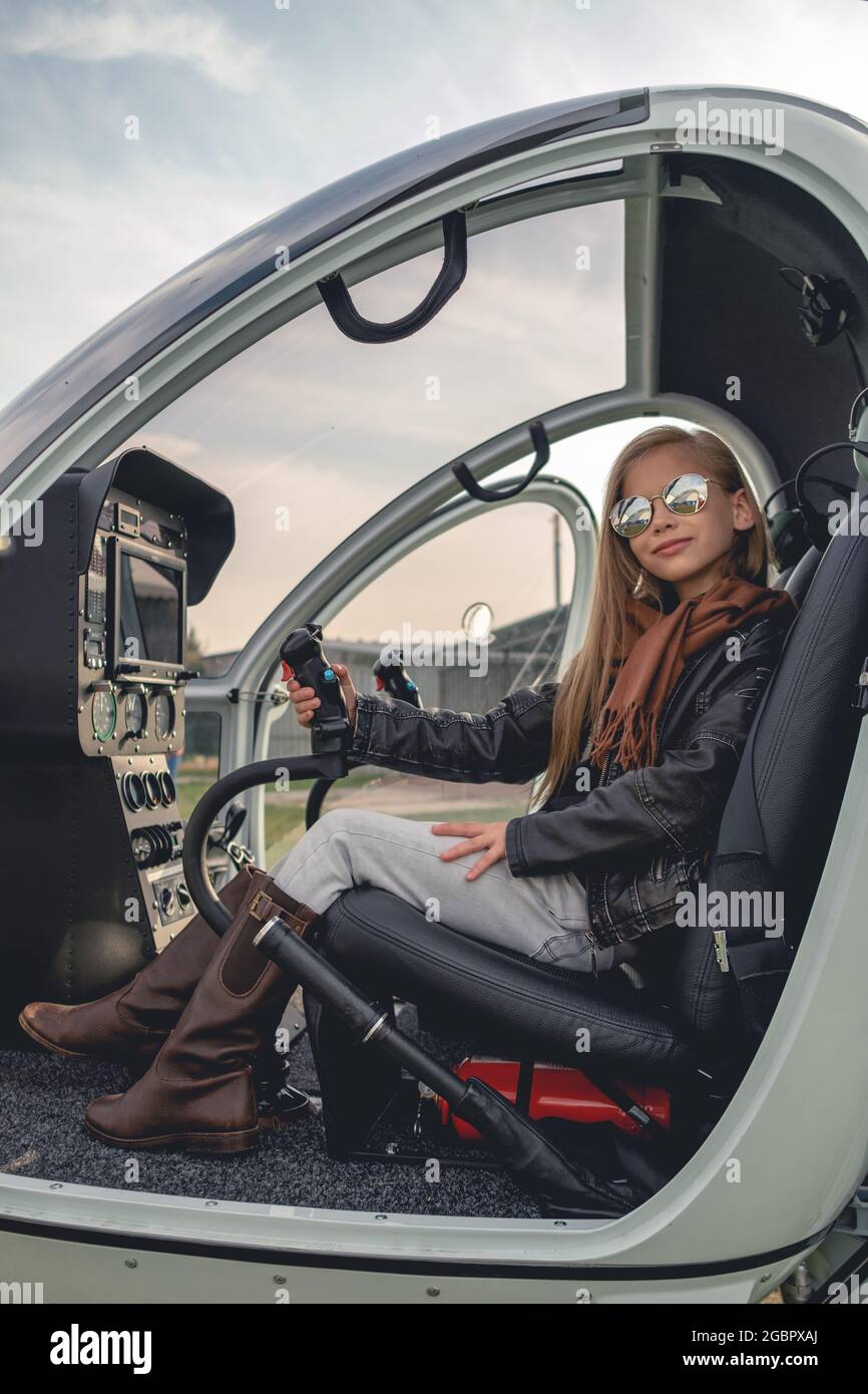 Sorridente ragazza Tween in occhiali da sole a specchio seduti in elicottero aperto Foto Stock