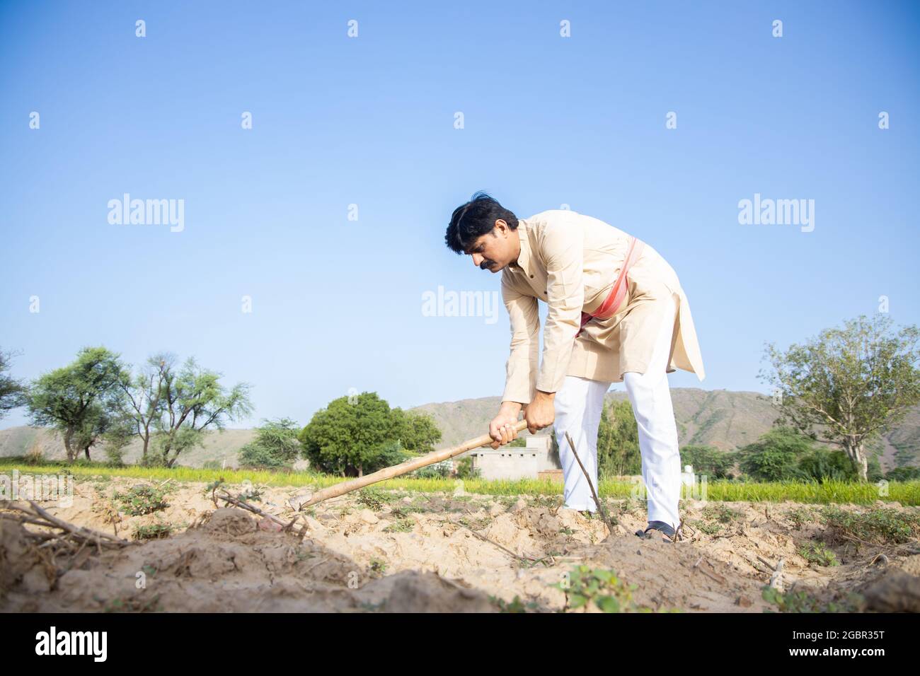 Coltivatore indiano scavando terreno agricolo, lavoro di uomo che lavora in campo agricolo con l'attrezzo agricolo. Lavorante duro maschio, cielo blu chiaro, spazio di copia, angolo basso, Foto Stock