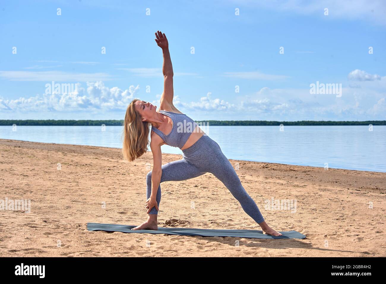 Donna sulla spiaggia in una giornata estiva è impegnata in esercizi fisici sullo sfondo del fiume, yoga Foto Stock