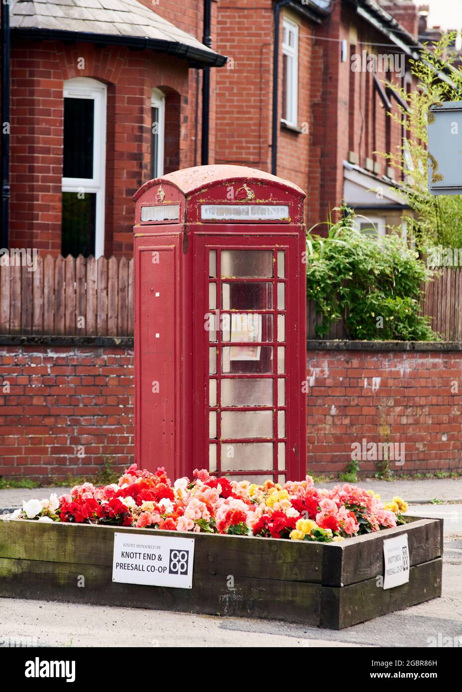 Vecchia scatola telefonica rossa e letto di fiori di fronte al rosso bricked terrazza fila di case Foto Stock