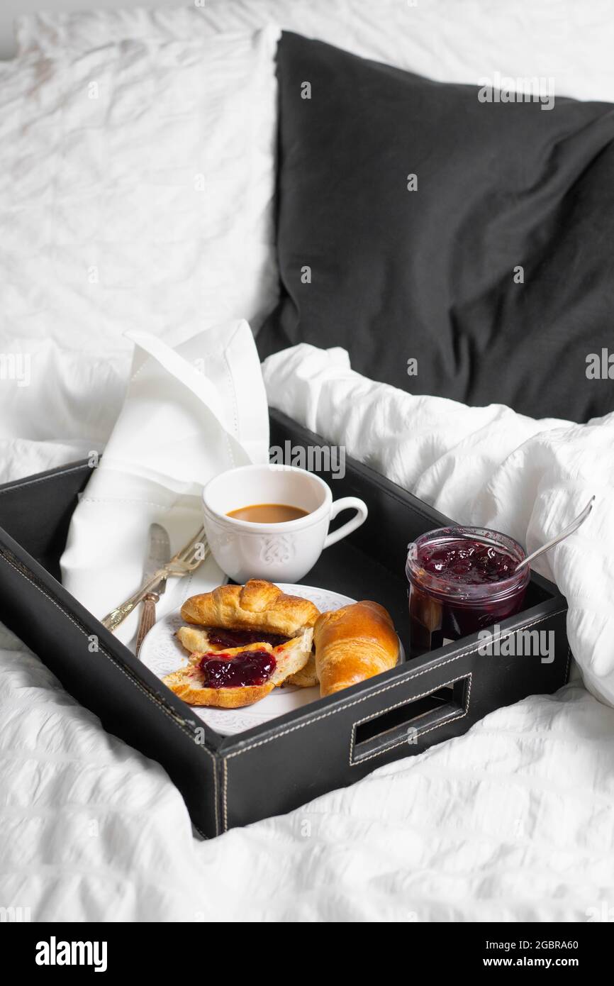 Colazione con croissant e tazza di caffè servita in un vassoio a letto con biancheria bianca. Foto Stock