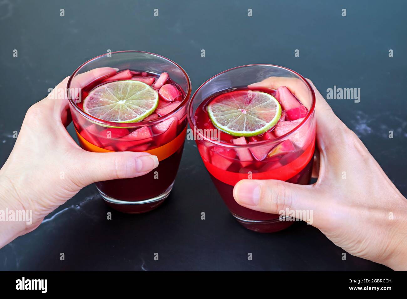 Donna e mano dell'uomo che tiene il bicchiere di vino rosso Sangria sul tavolo nero Foto Stock