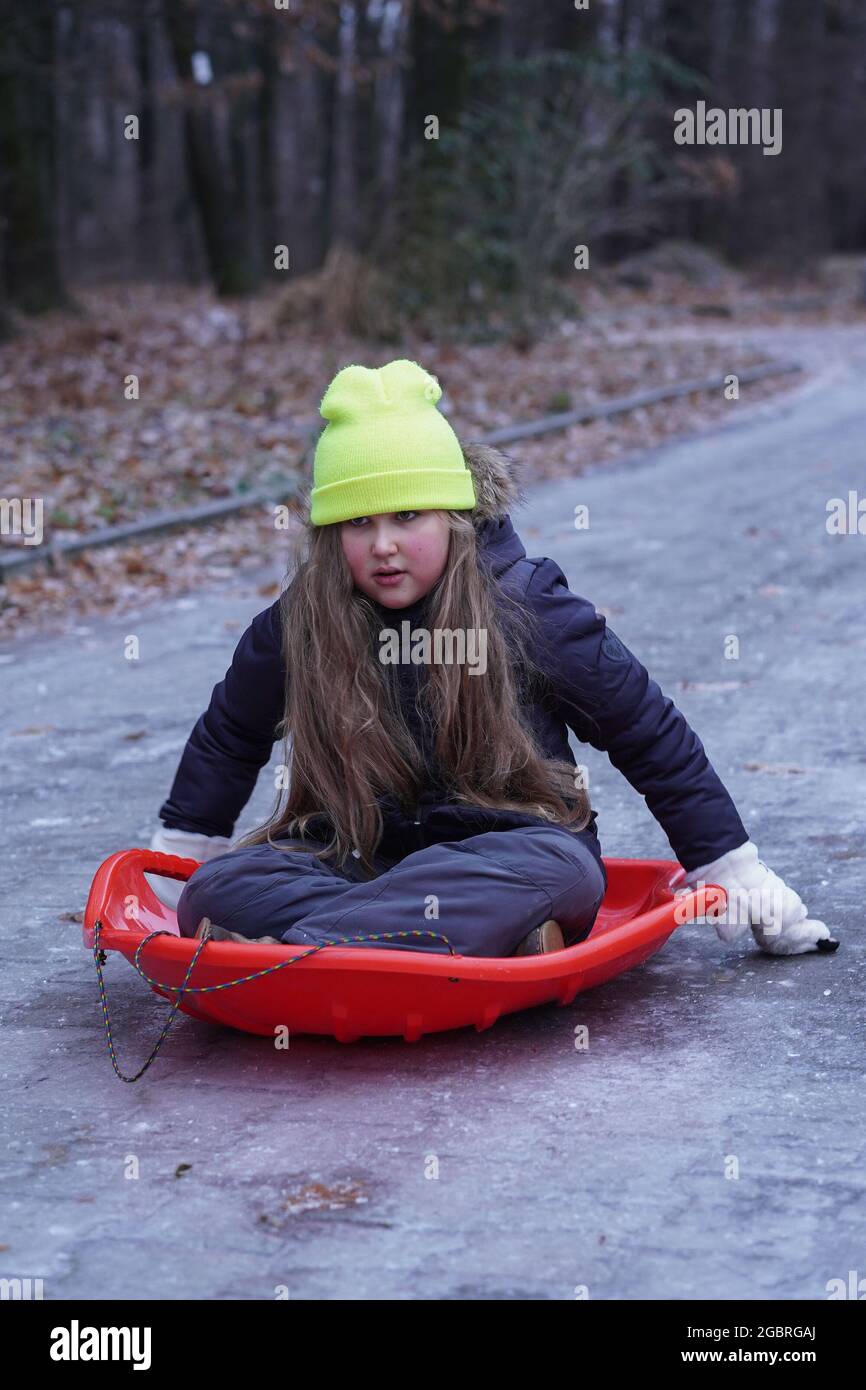 Infanzia, slittino e concetto di stagione - capretto divertente scivolando su una strada di ghiaccio dopo la pioggia ghiacciata vicino a casa in inverno. Condizioni atmosferiche della natura anomale. Foto Stock