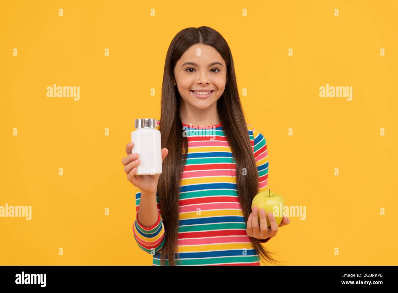 Happy ragazza bambino tenere mela e supplemento bottiglia sfondo giallo, vitamine Foto Stock