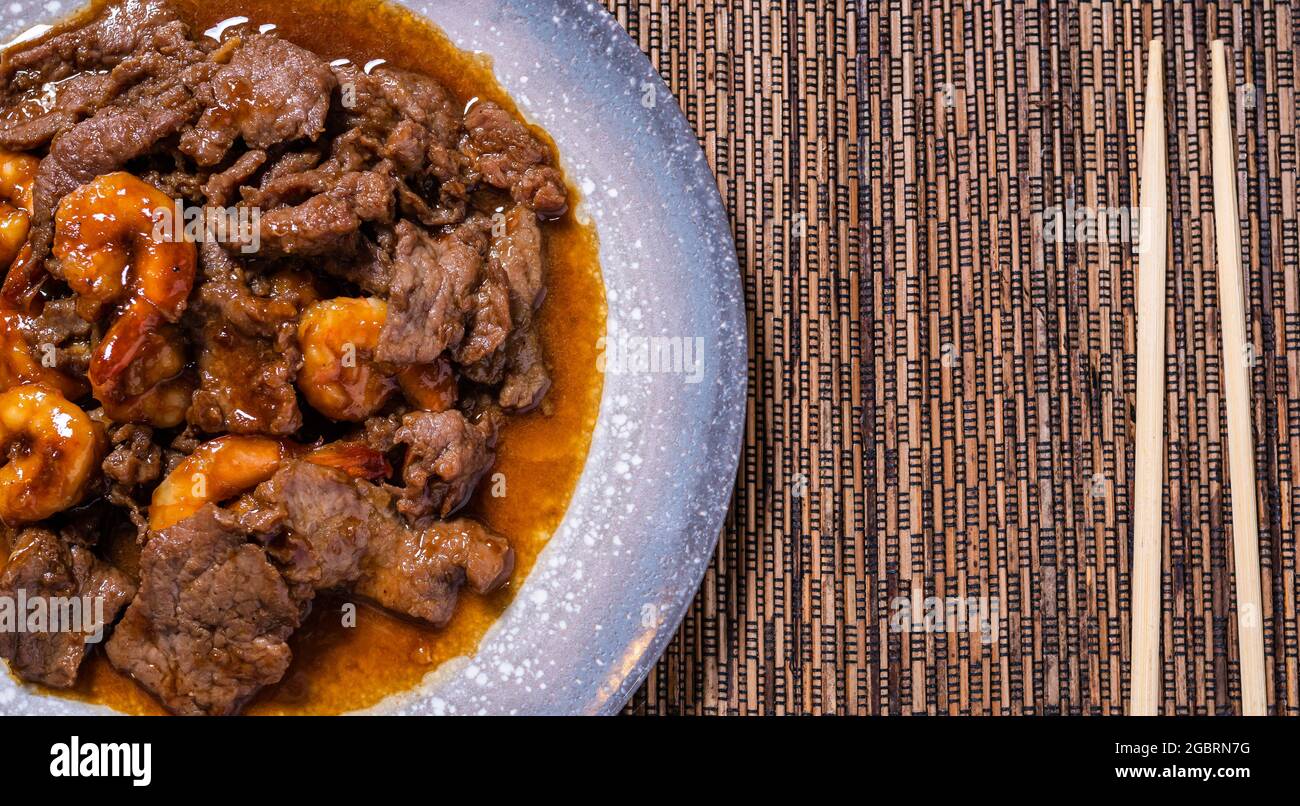 vista dall'alto del piatto orientale di manzo con gamberi e bastoncini sul lato. Cucina cinese e asiatica. Foto Stock