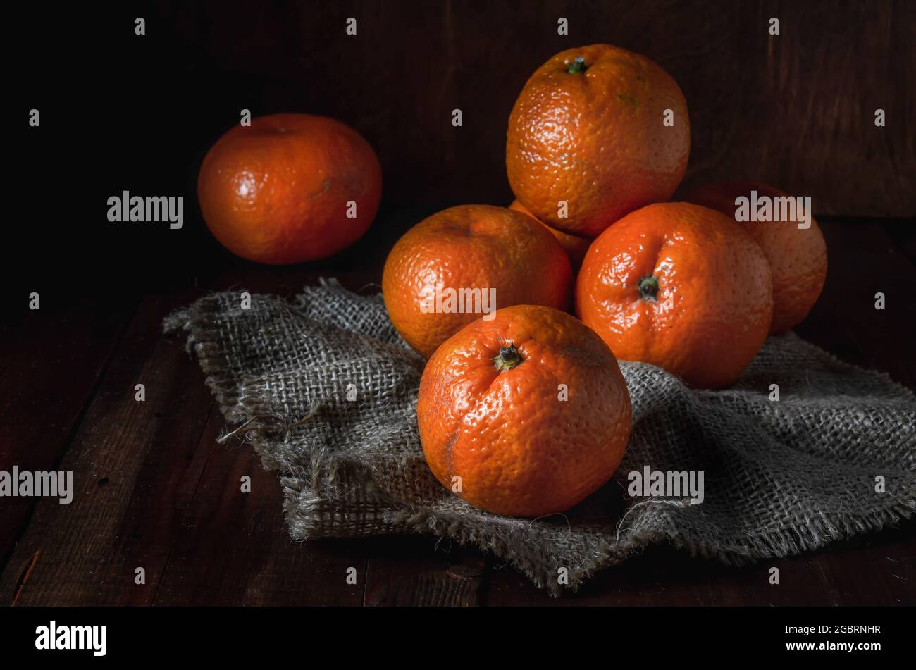 tangerini sfusi su un tessuto grosso, in uno stile rustico scuro Foto Stock