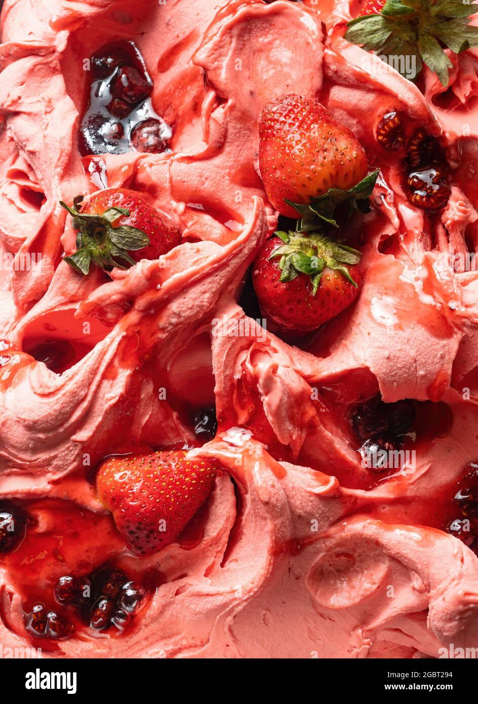 Gelato al gusto di fragola congelato - dettaglio a cornice. Primo piano di una superficie rosa di gelato coperto con pezzi di frutta rossa. Foto Stock