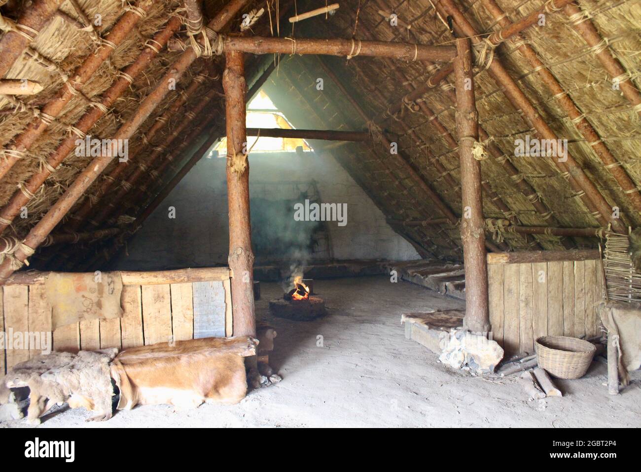 Butser Antica Fattoria - Vista interna della casa neolitica con fuoco aperto, pelli animali e zone notte. Foto Stock