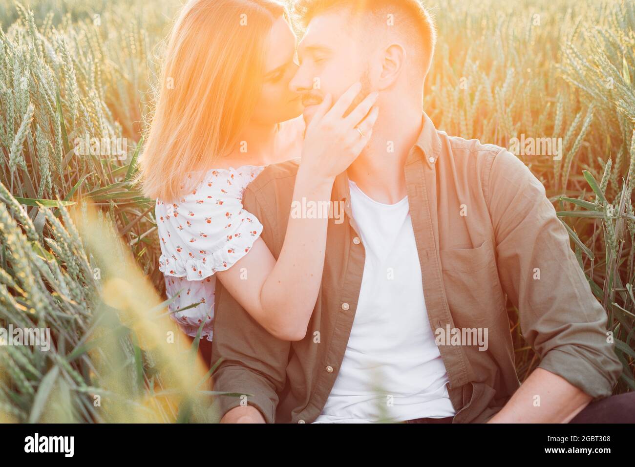 Bella giovane coppia irradia una tenerezza sconfinata l'una per l'altra seduta in campo tra erba alta . Amore e tenerezza. Bei momenti di vita Foto Stock