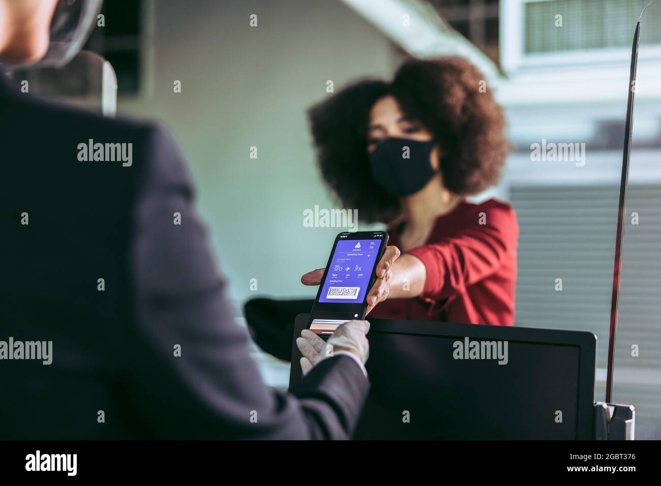 Una donna che indossa una maschera che mostra la carta d'imbarco elettronica al telefono per l'addetto a terra al banco del check-in presso il terminal dell'aeroporto durante il pandemi Foto Stock