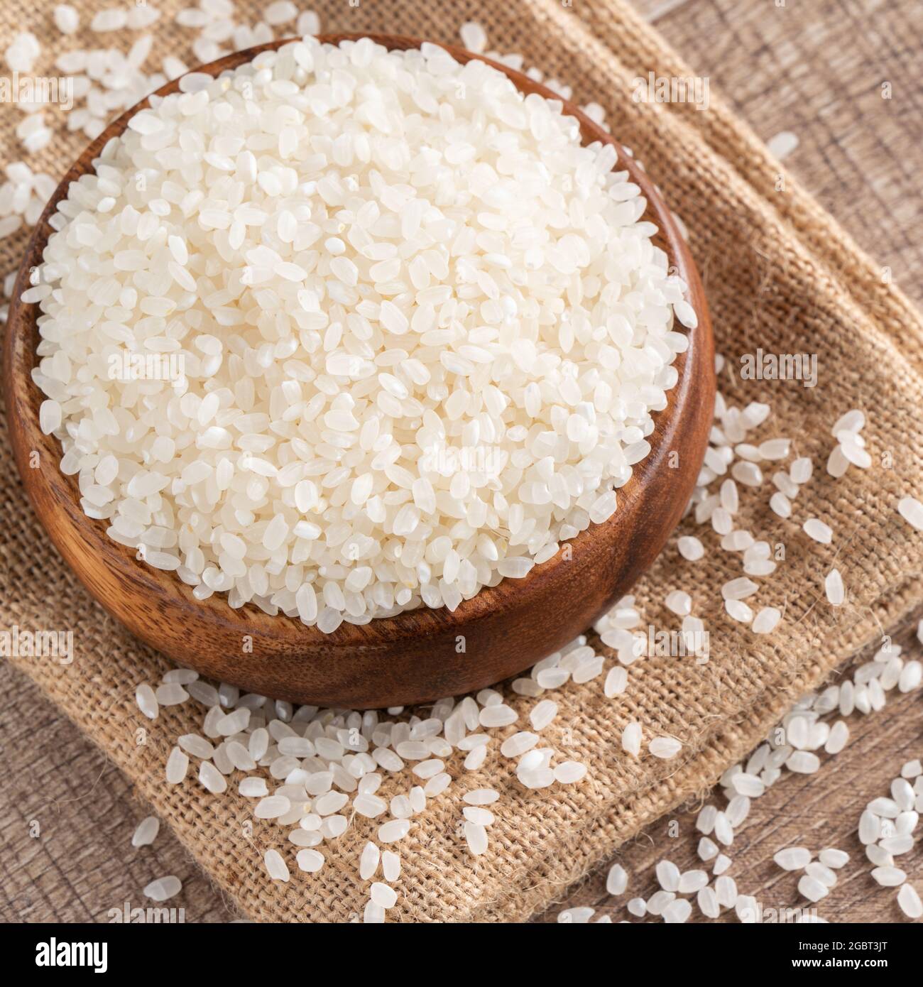 Riso bianco crudo macinato commestibile su fondo tavola di legno in una ciotola, concetto di design organico. Foto Stock