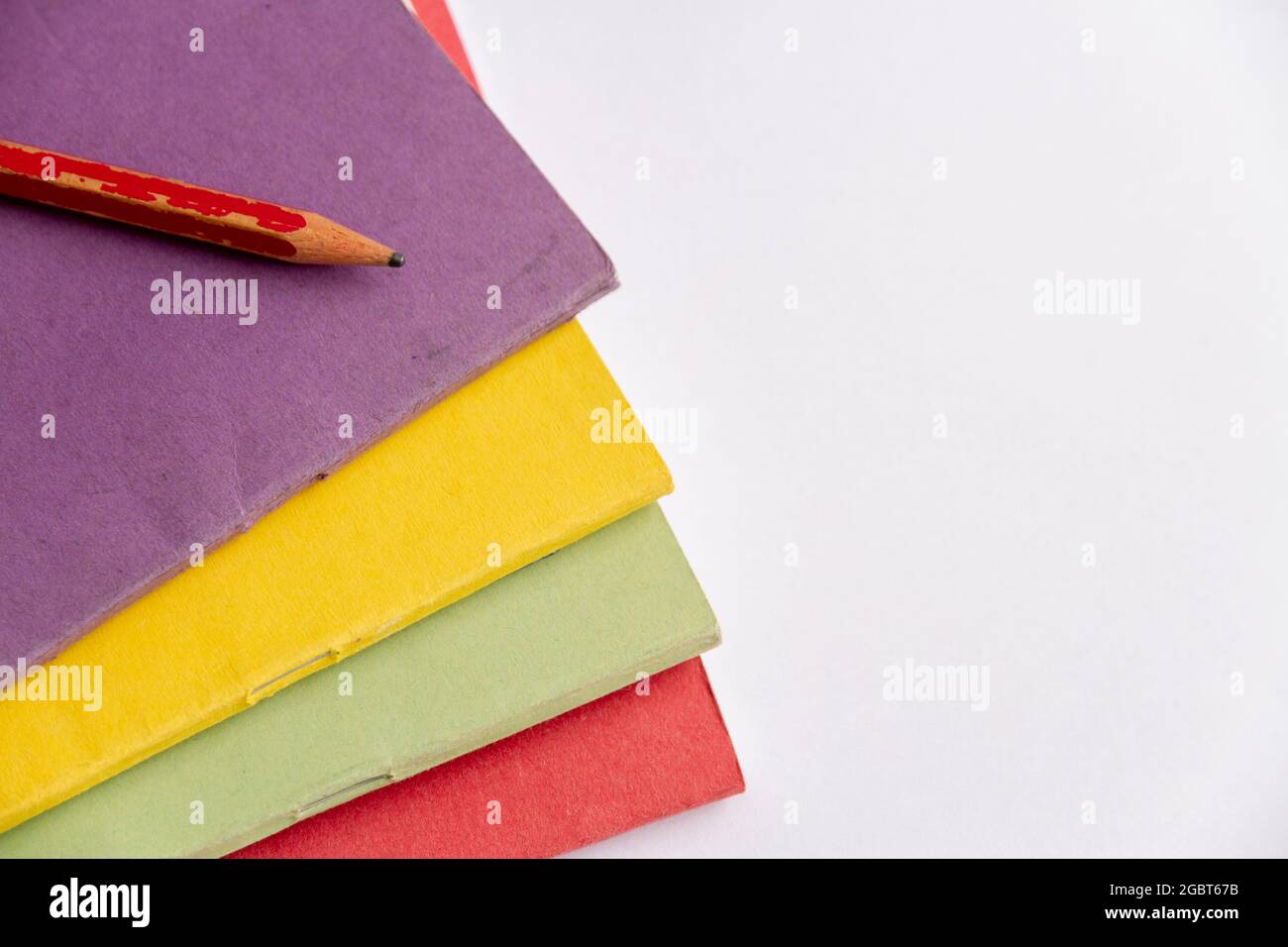 Foto in alto di una matita sulla parte superiore di un mucchio di libri di note colorati. Formato orizzontale, sfondo neutro, spazio per il testo Foto Stock