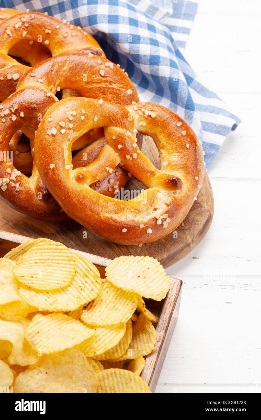 Pretzel fatto in casa appena sfornato con sale marino e patatine su tavolo di legno. Classico spuntino con birra Foto Stock