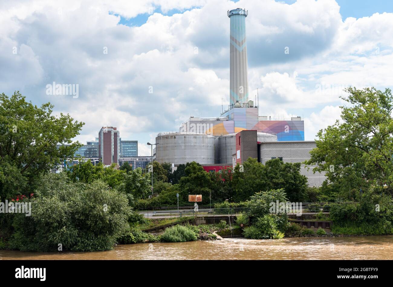 Vista di un impianto di cogenerazione lungo il fiume che prudono il riscaldamento e l'elettricità in una giornata estiva parzialmente nuvolosa Foto Stock