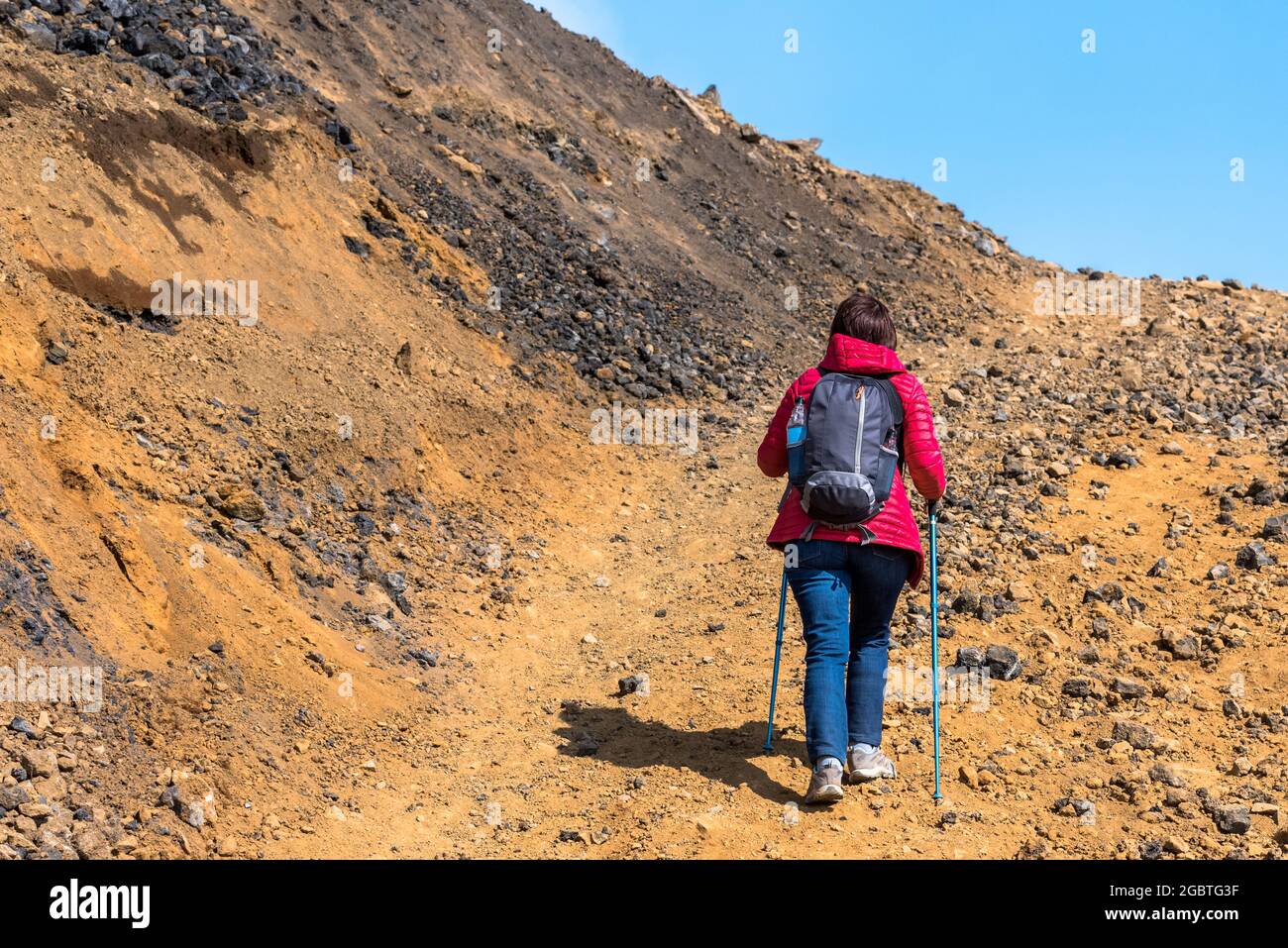 Donna escursionista che arrampica su una ripida pista di montagna con l'aiuto di pali escursionistici in Islanda in una soleggiata giornata estiva Foto Stock