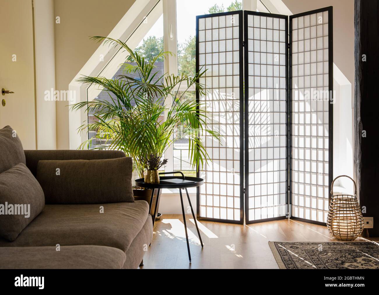 Soggiorno domestico con schermo divisorio in legno e carta che blocca il sole dalla finestra, tavolo in metallo nero e divano, colori naturali. Foto Stock