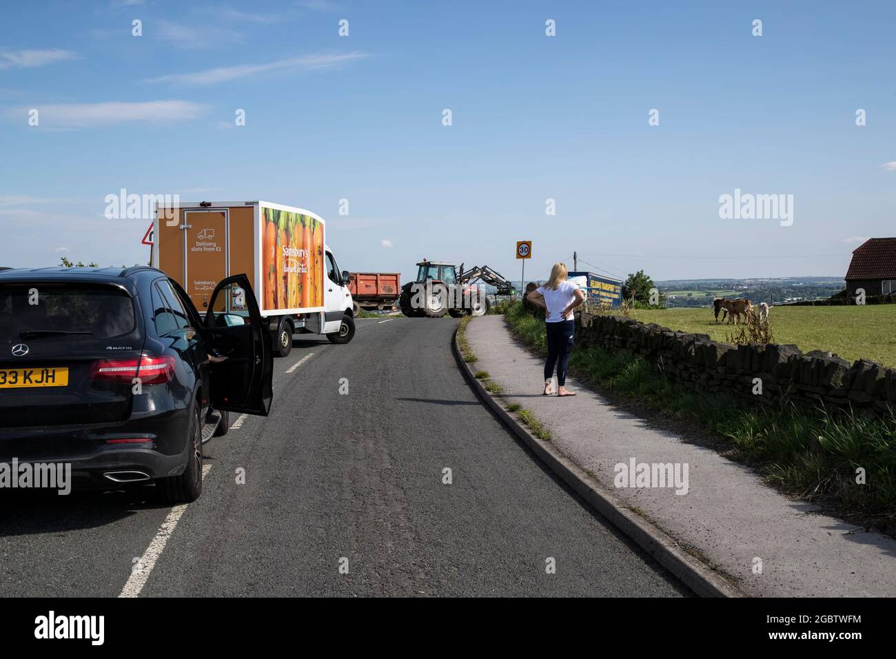 Il traffico si è fermato su una strada di campagna negli uplands dello Yorkshire, in Inghilterra, per consentire al bestiame e a un trattore di attraversare la strada Foto Stock