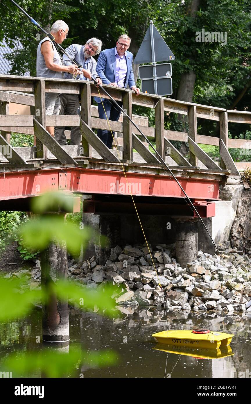 05 agosto 2021, Brandeburgo, Fehrbellin: Il Ministro dell'ambiente Axel Vogel (Bündnis 90/Die Grünen - M) e Mathias Perschall (SPD - r), sindaco di Fehrbellin, imparano a conoscere la misurazione del flusso e l'acquisizione dei dati nel canale del Reno da Lothar Nowak dell'Agenzia statale dell'ambiente presso la stazione di misura di livello Fehrbellin. Un'imbarcazione di misurazione viene utilizzata per misurare automaticamente il flusso. In un viaggio di stampa nella brughiera agricola del Rhinluch, Vogel impara circa la protezione di clima attraverso la gestione della brughiera e un equilibrio migliore dell'acqua del paesaggio. Foto: Jens Kalaene/dpa-Zentralbild/dpa Foto Stock