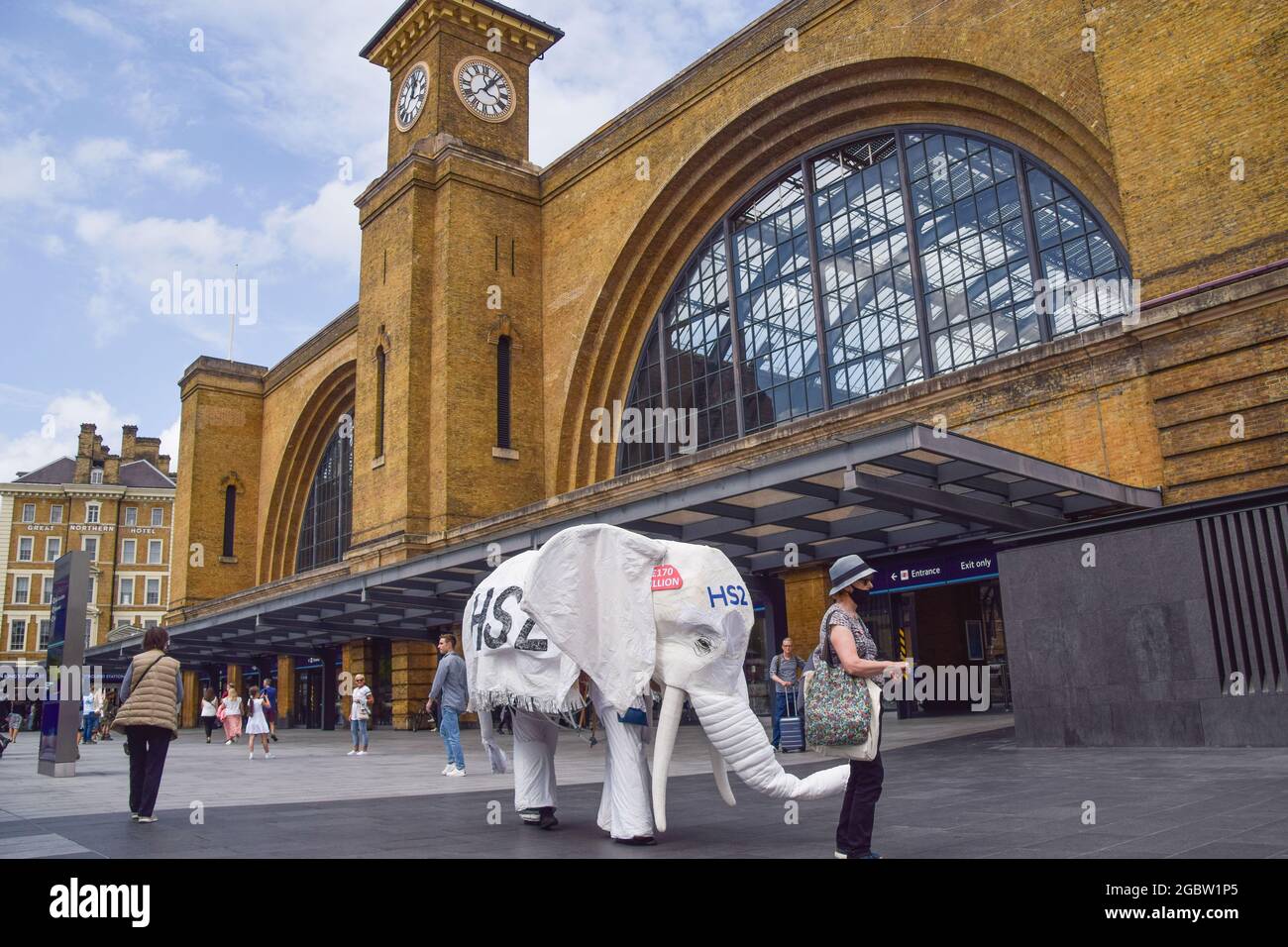 Londra, Regno Unito. 5 agosto 2021. I manifestanti che indossano un costume da elefante bianco 'HS2' sono condotti fuori dalla stazione ferroviaria da un altro protestore. Gli attivisti si sono riuniti fuori dalla King's Cross Station per protestare contro il nuovo sistema ferroviario ad alta velocità 2 (HS2), che gli ambientalisti dicono sarà 'ecologicamente devastante' e costerà ai contribuenti £170 miliardi. (Credit: Vuk Valcic/Alamy Live News) Foto Stock