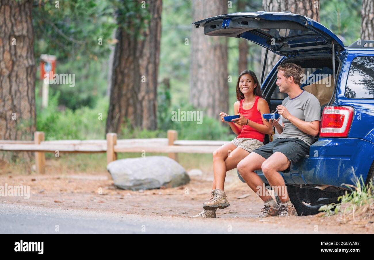 Viaggio su strada turista coppia mangiare pranzo cibo sul retro dell'auto in estate campeggio vacanza viaggio. Gente di guida felice Foto Stock