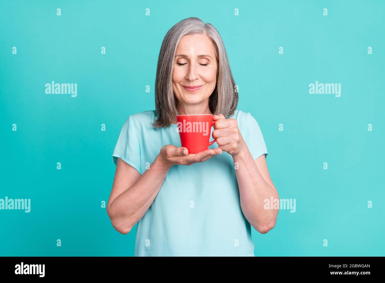 Foto di affascinante nonna sognante con gli occhi chiusi odore caffè caffeina amante isolato su sfondo turchese Foto Stock
