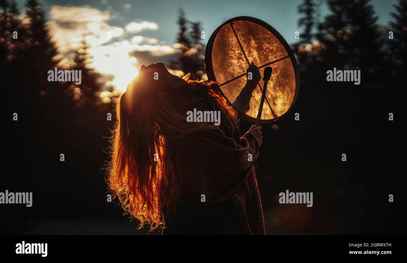 Bella ragazza sciamanici giocando sul telaio sciamano tamburo nella natura. Foto Stock