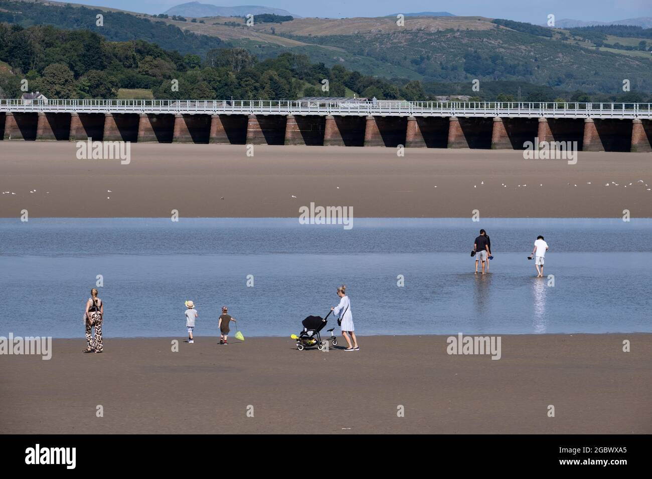 I vacanzieri di Arnside, nel Lancashire, Inghilterra, durante le vacanze estive, hanno fatto marea sull'oceano lasciando una striscia di acqua tra due spiagge sabbiose. Foto Stock