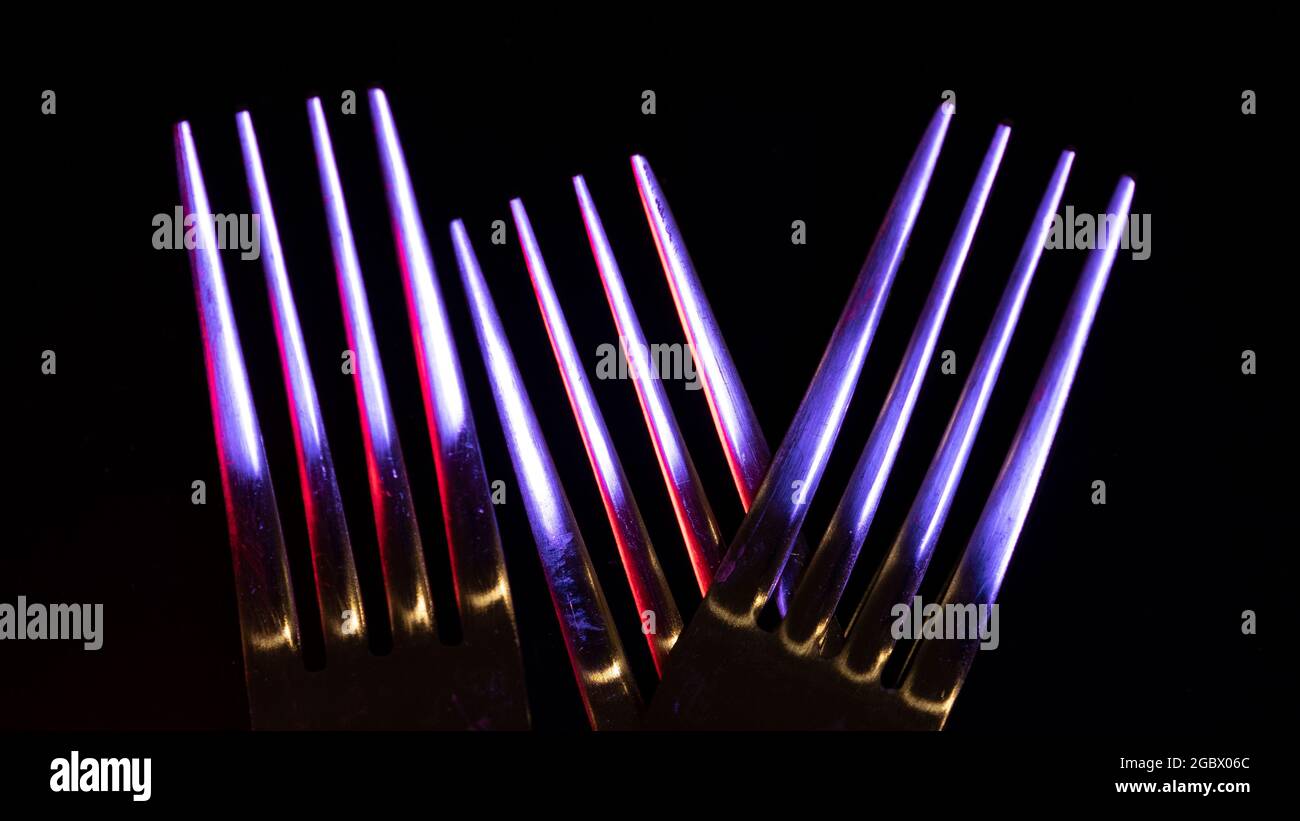 Primo piano di tre forcelle lucide su sfondo nero illuminate da luci colorate che fanno un'immagine astratta Foto Stock