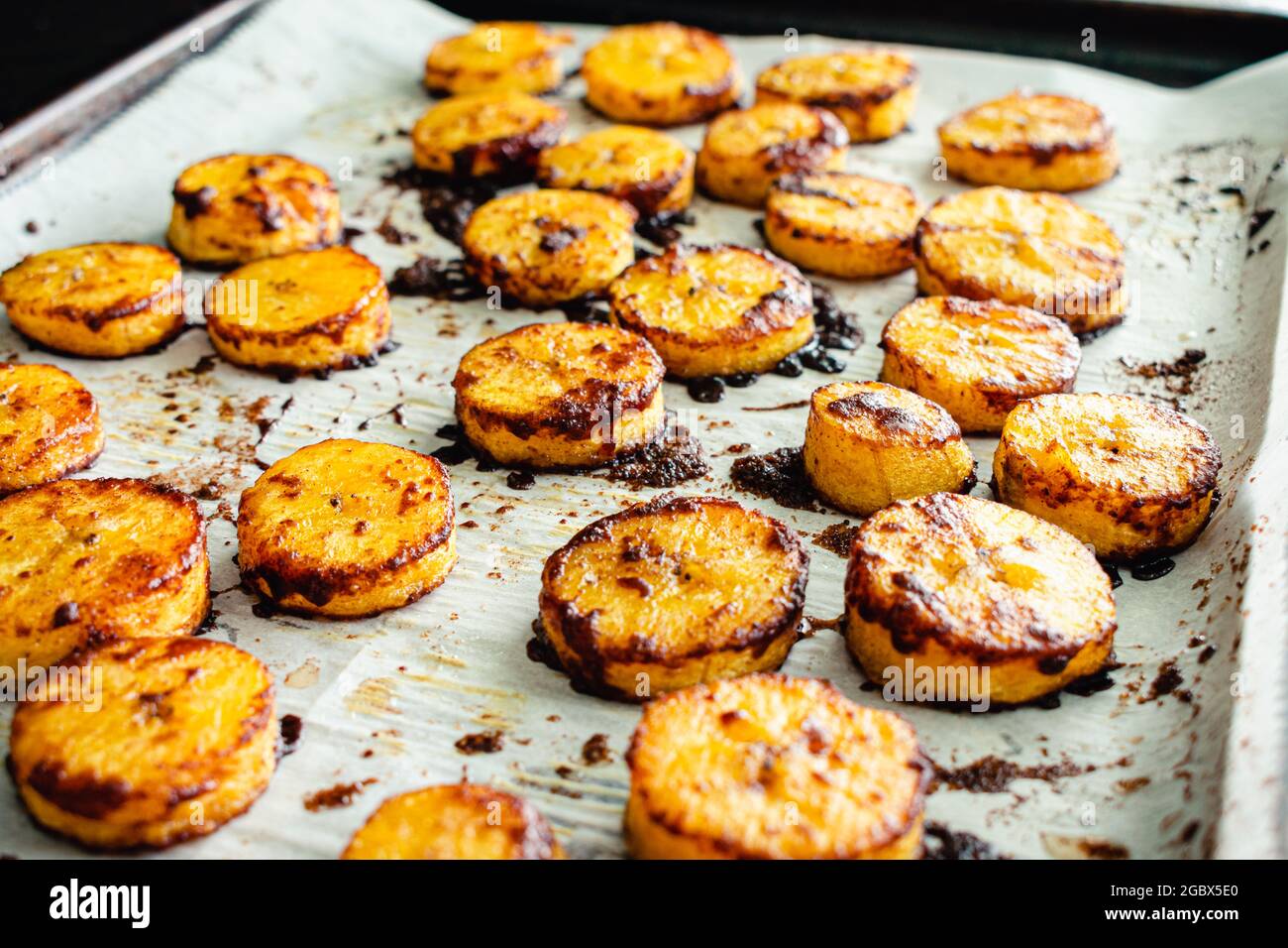 Piantane cotte alla cannella dolce al caramello: Una padella di foglie ricoperte di pergamena di plantani cotti ricoperti di cannella e zucchero caramellato Foto Stock