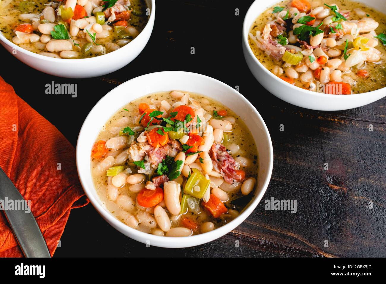 Ciotole di fagioli bianchi e zuppa di prosciutto con pane: Tre ciotole di zuppa di fagioli cannellini con maiale affumicato e verdure Foto Stock