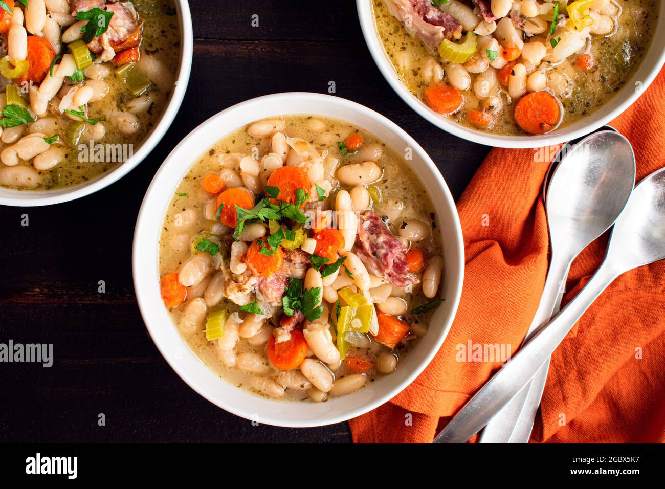 Ciotole di fagioli bianchi e zuppa di prosciutto con pane: Tre ciotole di zuppa di fagioli cannellini con maiale affumicato e verdure Foto Stock