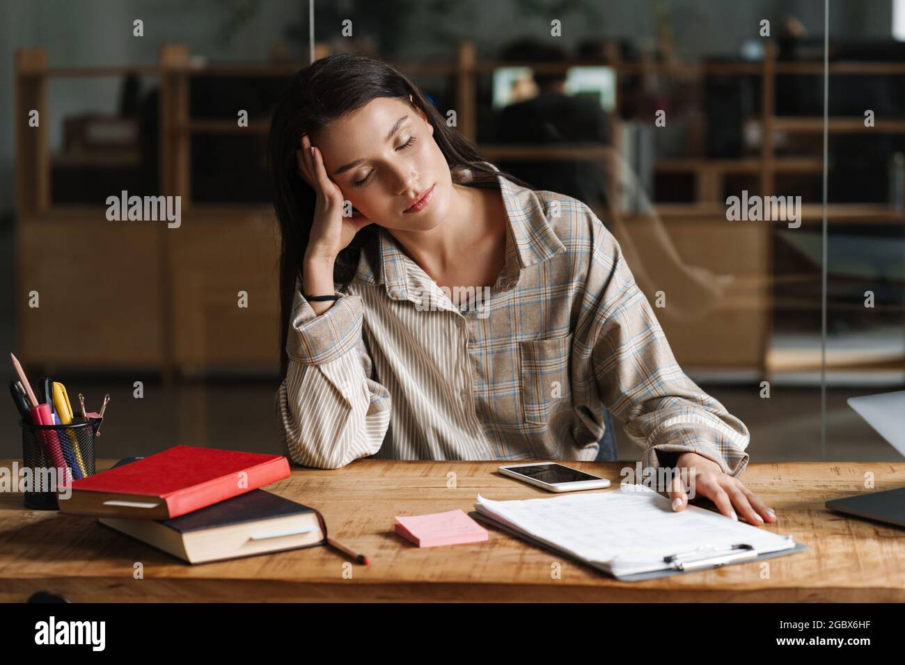 Giovane stanca donna bianca brunetta casual seduta dormendo alla scrivania dell'ufficio con gli occhi degli appunti chiusi Foto Stock