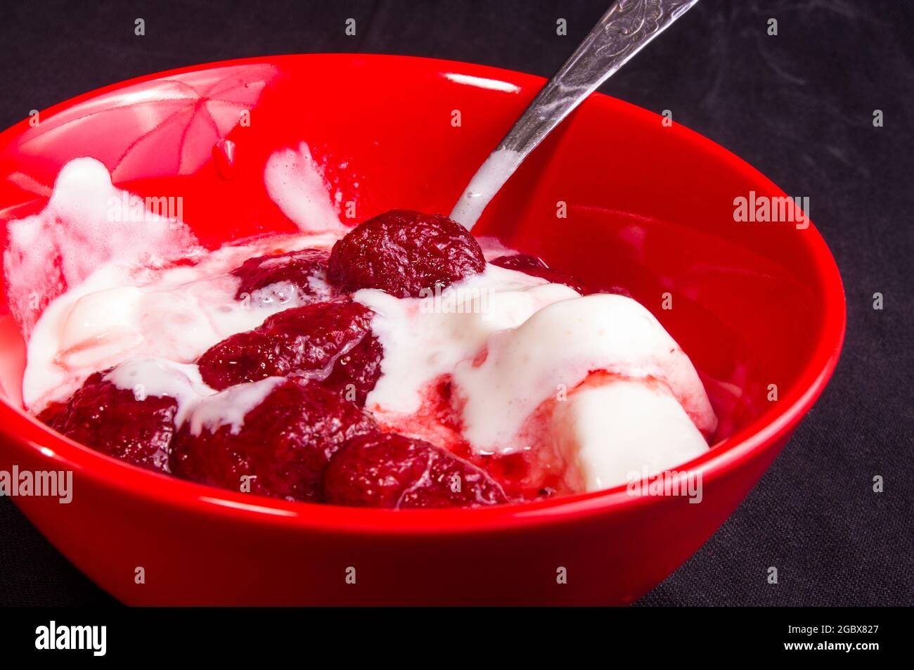 Dolce dessert - gelato cremoso con marmellata di fragole in ciotola rossa su sfondo nero, primo piano Foto Stock