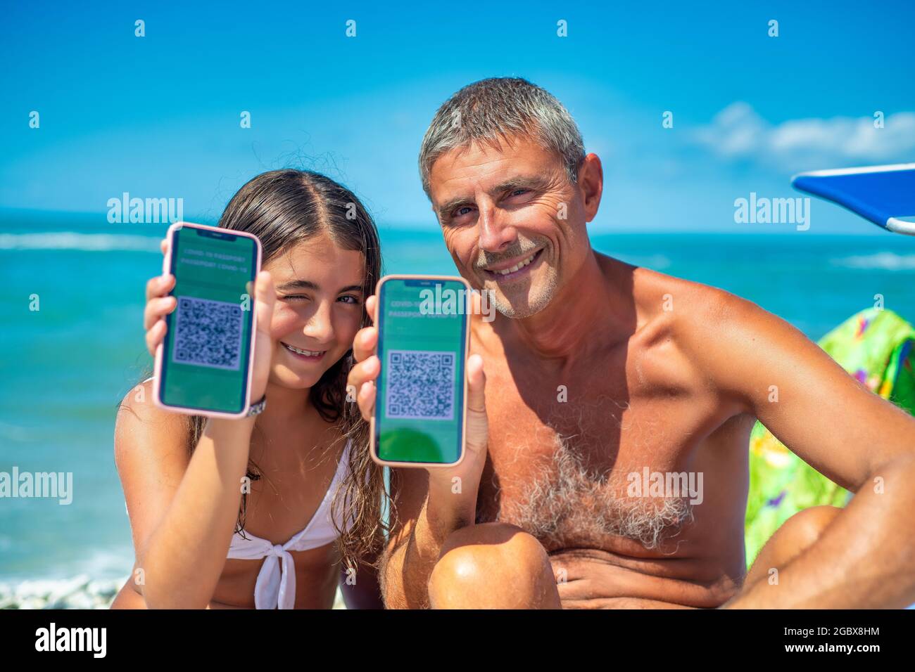 Felice famiglia sulla spiaggia con covid green pass. Uomo e figlia di 10 anni pronti a fare un viaggio con screenshot della vaccinazione Foto Stock