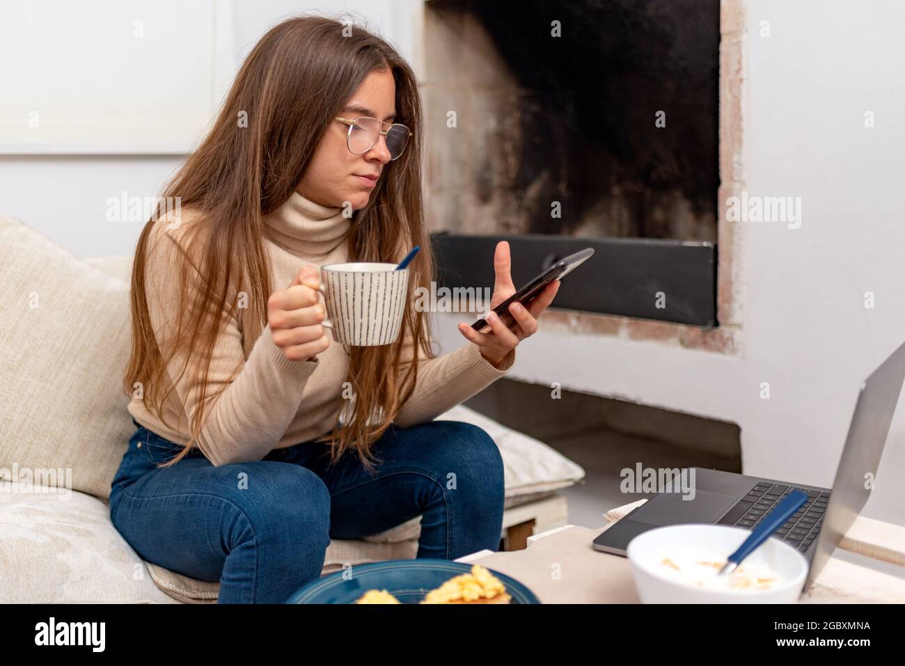 Giovane donna latina che usa il telefono cellulare mentre si serve la colazione a casa. Foto Stock