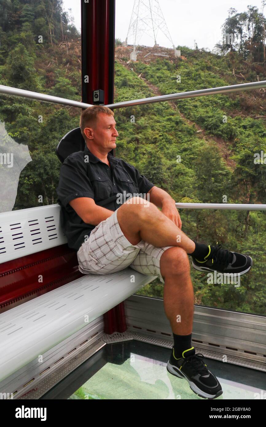 Terra vista attraverso il pavimento in vetro di una Crystal Cabin. Uomo in cabina di funivia con pavimento in vetro. Gite turistiche sulla funivia. Genting Highland Foto Stock