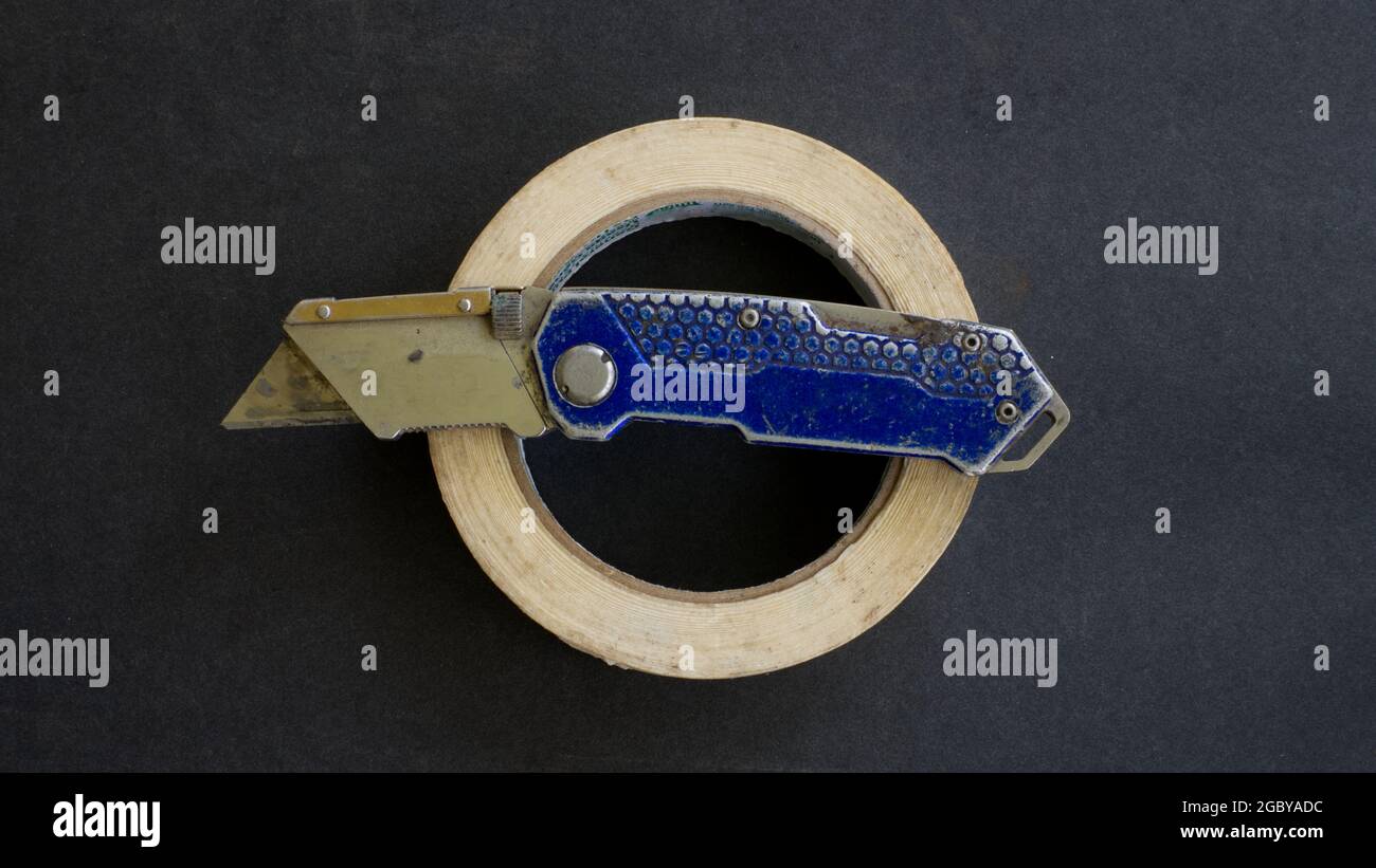 Un coltello e un nastro di mascheratura per uso generico su sfondo nero Foto Stock Un coltello e un nastro di mascheratura per uso generico su sfondo nero Foto Stock